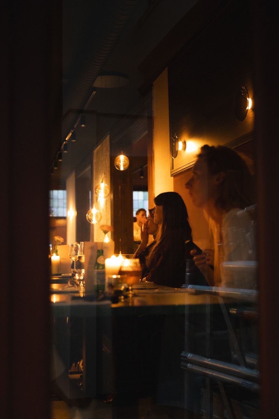 Gasten aan de bar bij kaarslicht, gezien door het raam